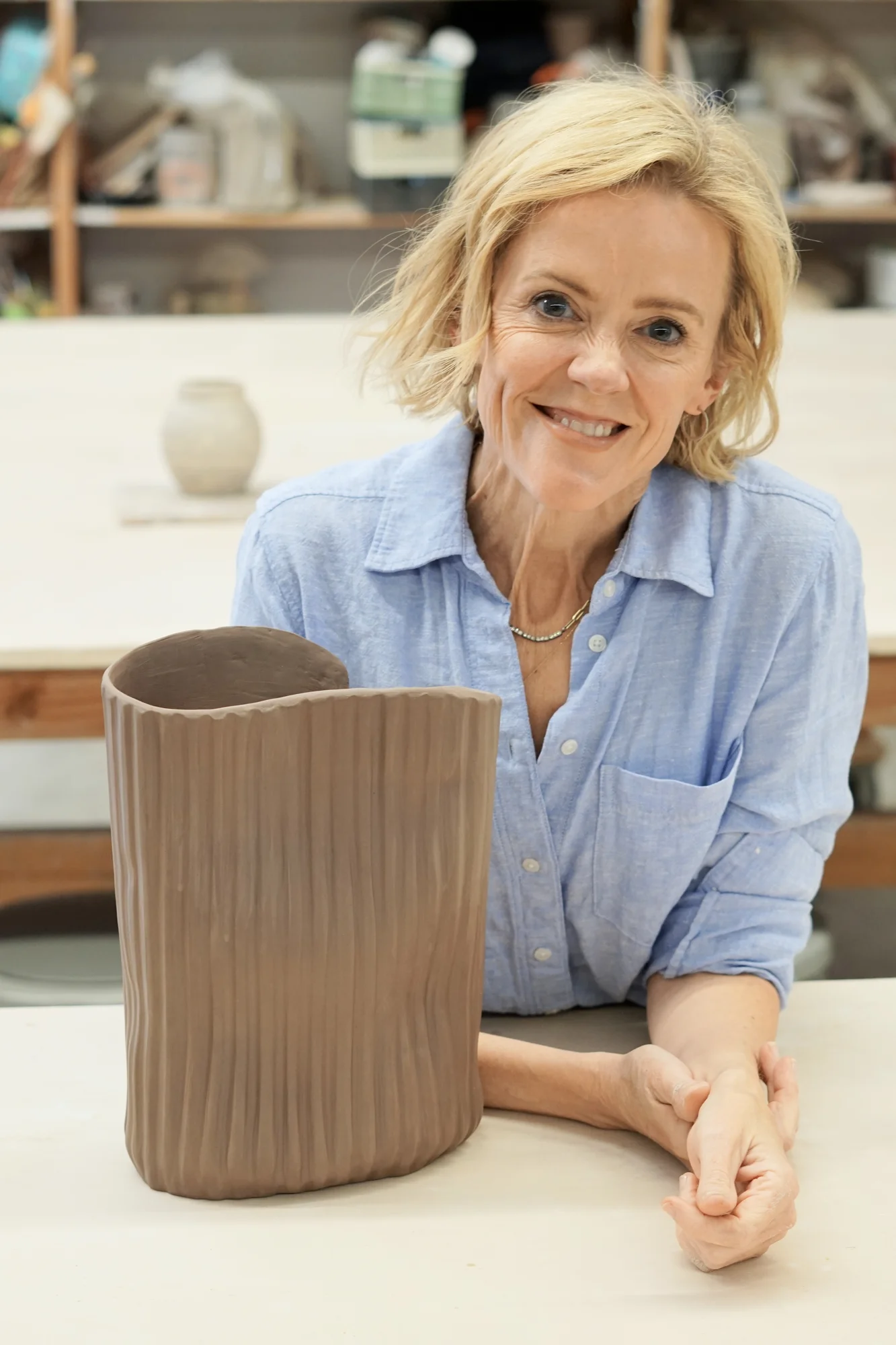 Krysta at the studio table beside a large textured, iron-rich vase