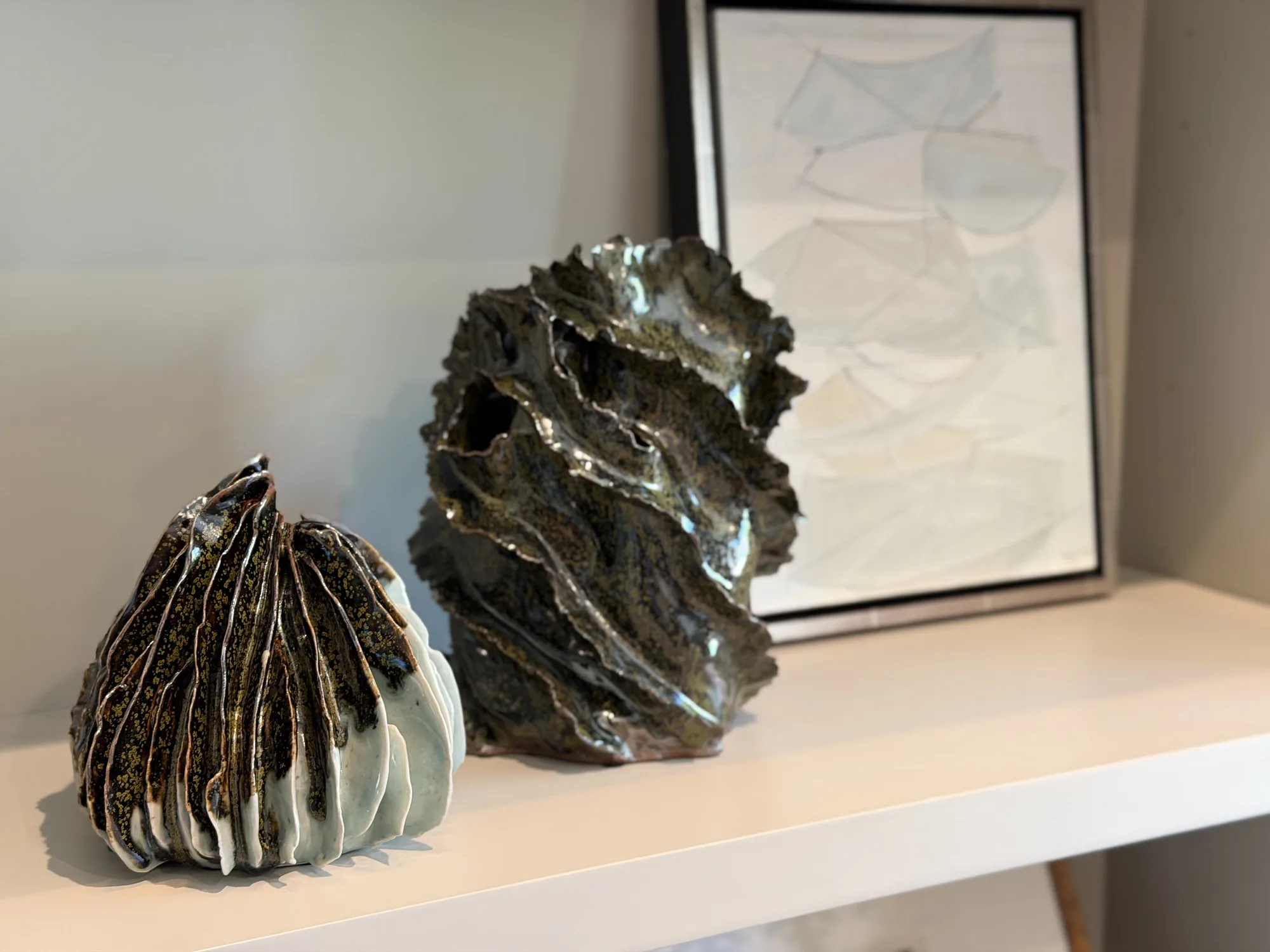 Two sculptural Krysta Mae vessels on a shelf beside a framed ink drawing