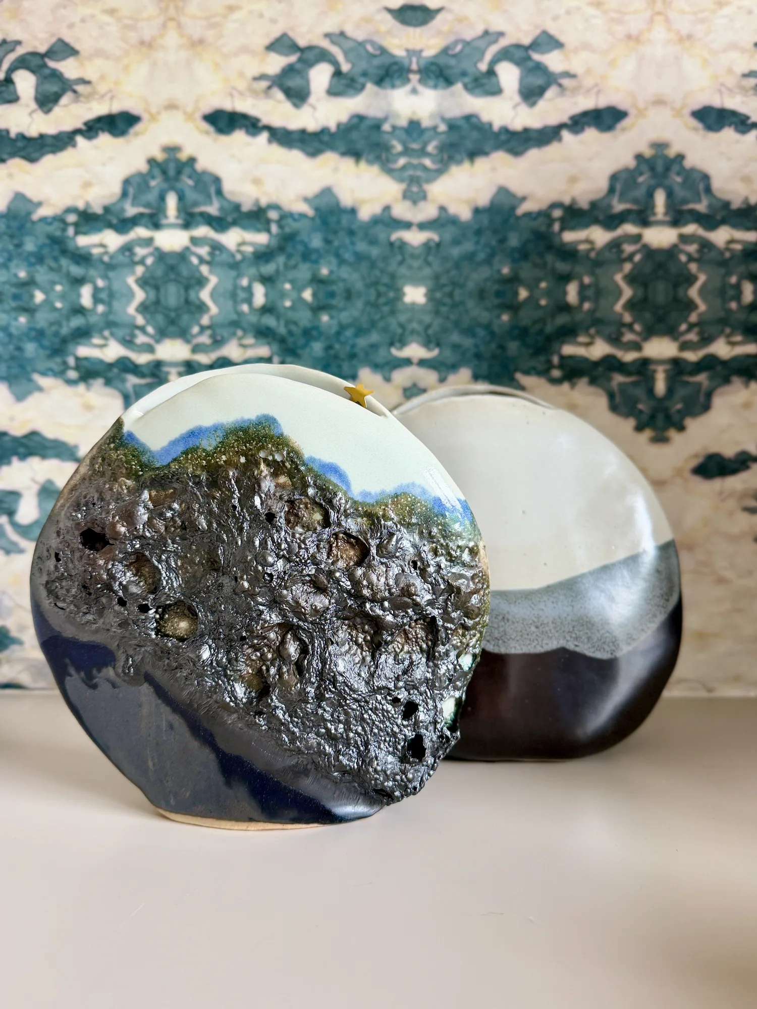 Lunar Disk No. 3, a dark textured ceramic disc, against patterned wallpaper
