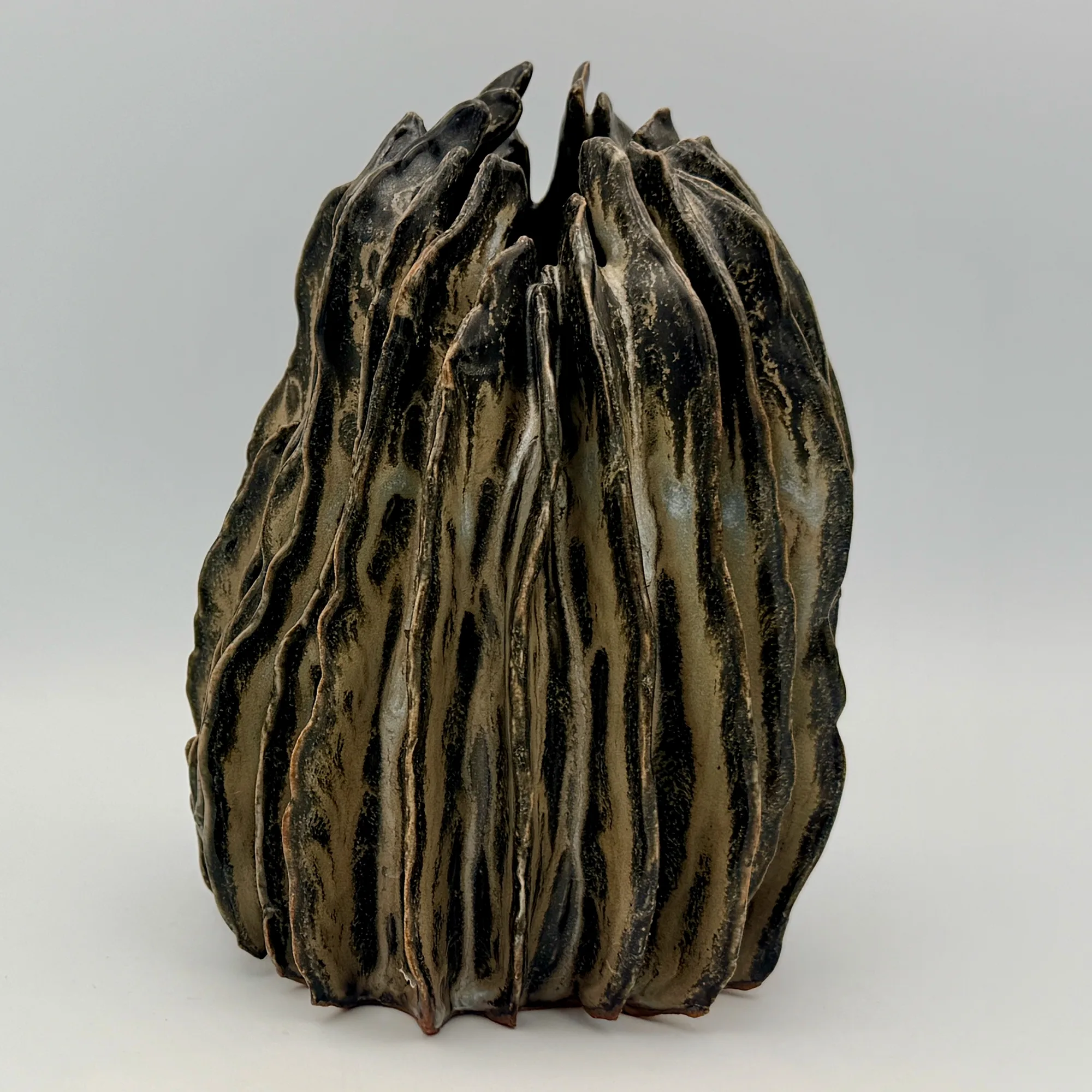 A dark stoneware vessel with deep vertical folds rising to a jagged, open rim